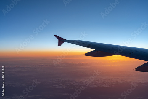 Up in the air, view of aircraft wing silhouette with dark blue sky horizon and cloud background in sun rise or sunset time from airplane window.