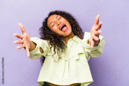 Young hispanic woman isolated on purple background feels confident giving a hug to the camera.