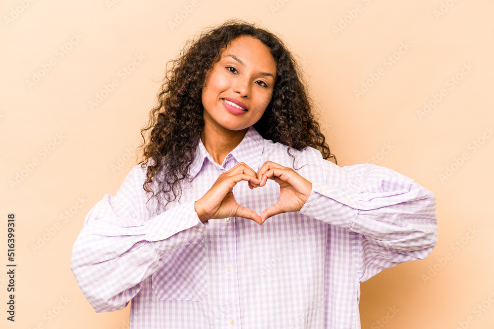 Young hispanic woman isolated on beige background smiling and showing a heart shape with hands. Young hispanic woman isolated on beige background smiling and showing a heart shape with hands.