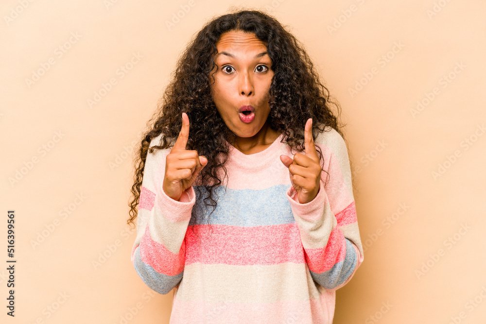 Young hispanic woman isolated on beige background pointing upside with opened mouth. Young hispanic woman isolated on beige background pointing upside with opened mouth.