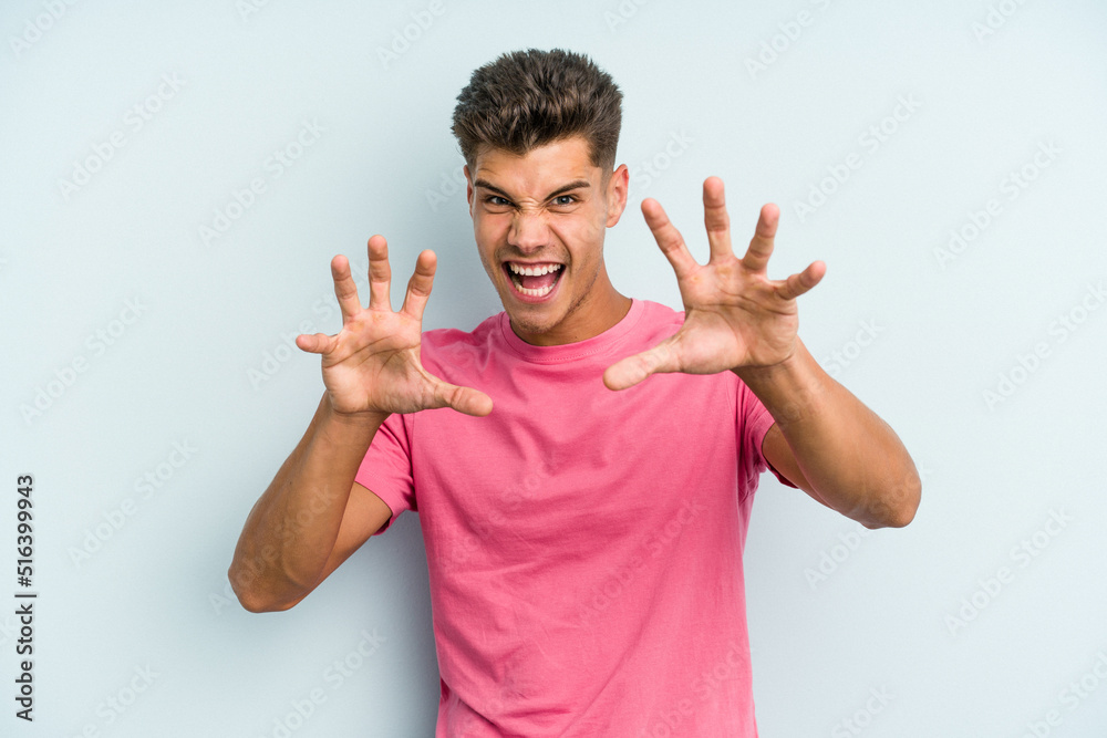 Young caucasian man isolated on blue background showing claws imitating a cat, aggressive gesture.