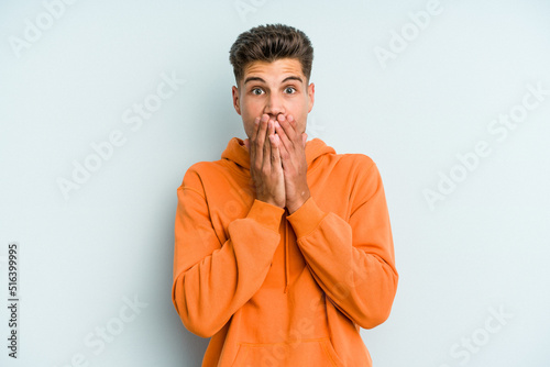 Young caucasian man isolated on blue background shocked covering mouth with hands.