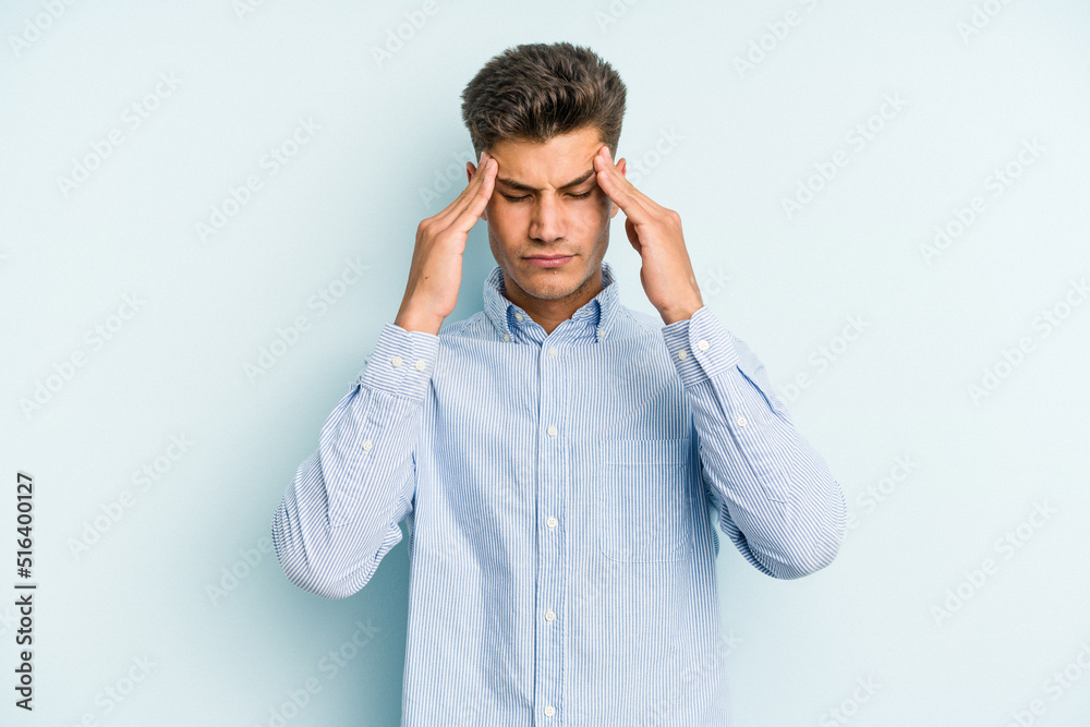 Young caucasian man isolated on blue background having a head ache, touching front of the face.