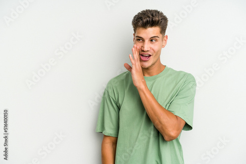 Young caucasian man isolated on white background is saying a secret hot braking news and looking aside