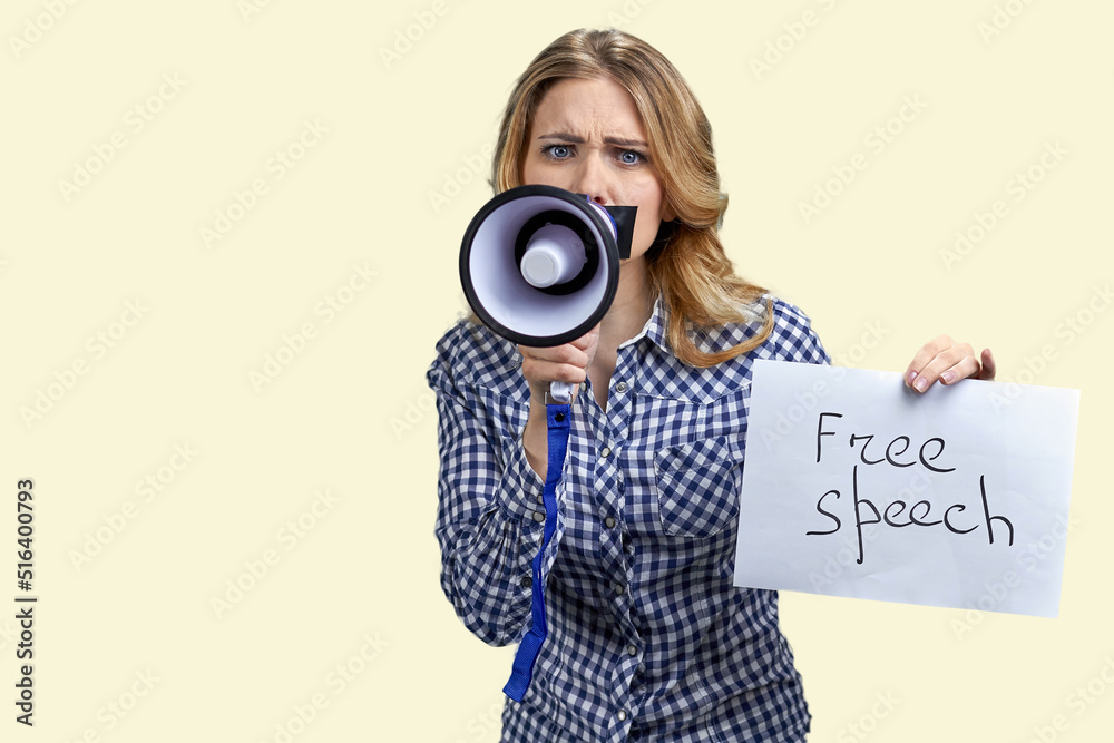 Fototapeta premium Upset woman protester with adhesive tape over mouth trying to speak in megaphone. Isolated on white background. Free speech.