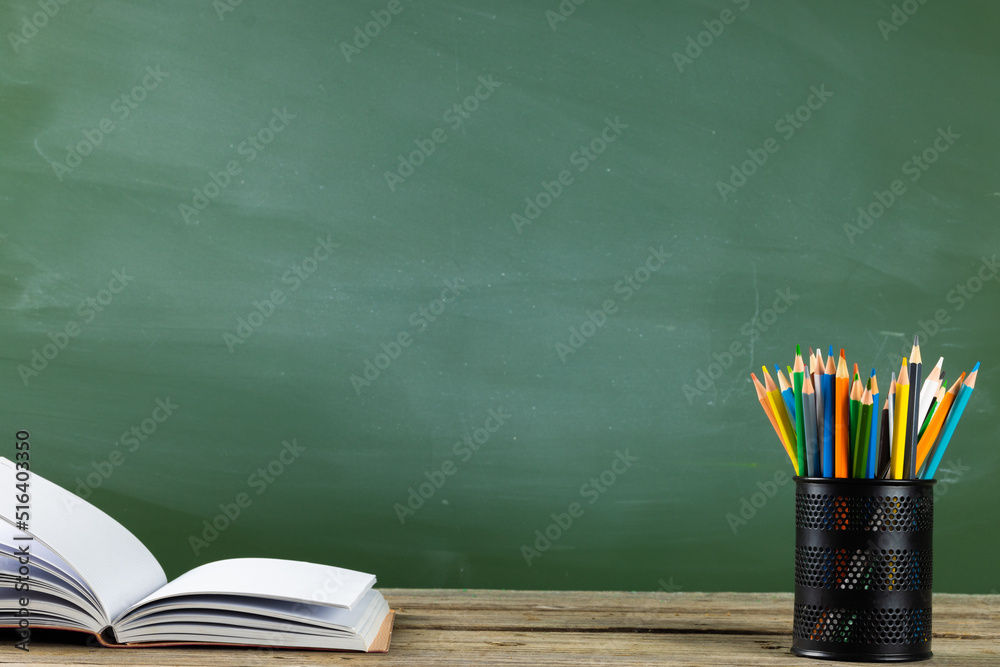 Image of books, notebook and crayons on wooden table over black board Image of books, notebook and crayons on wooden table over black board