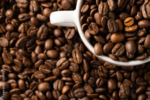 Image of white cup full of coffee beans on pile of coffee beans