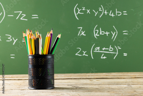 Image of cup with crayons over mathematical formulas on black board