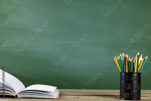 Image of books, notebook and crayons on wooden table over black board