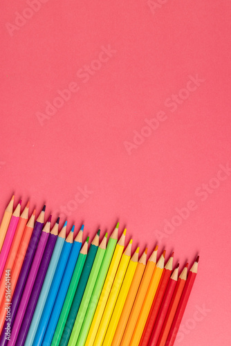 Vertical composition of colorful crayons on pink surface with copy space