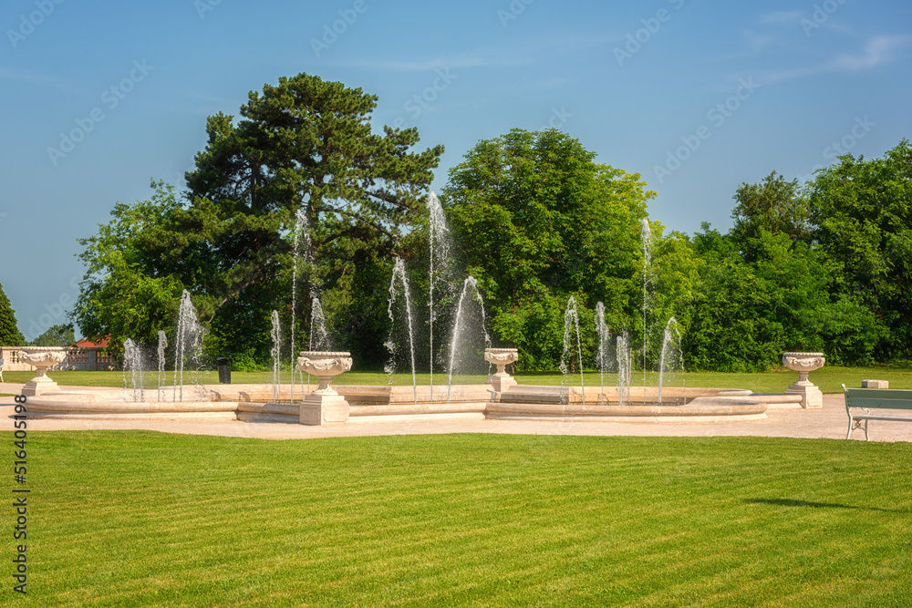 Beautiful garden of Festetics Palace with green grass and trees, decorative fountain and blue sky on a sunny summer day, Keszthely, Zala, Hungary. Outdoor travel background