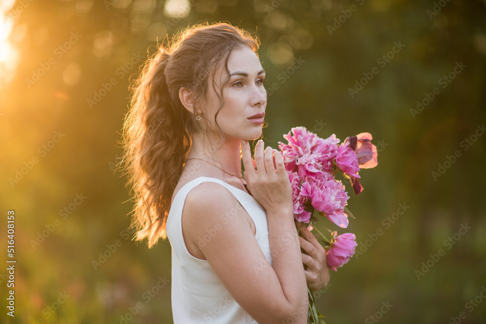 Fototapeta premium Beautiful happy young girl with peonies in nature outdoors in the sun. Beautiful woman in a field with flowers in a long skirt