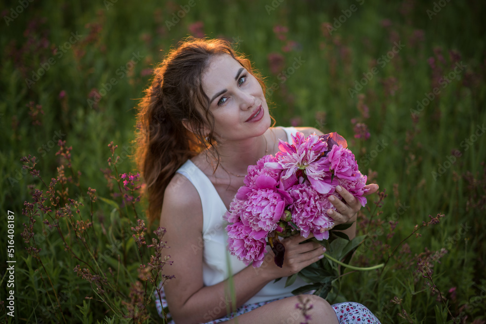 Fototapeta premium Beautiful happy young girl with peonies in nature outdoors in the sun. Beautiful woman in a field with flowers in a long skirt