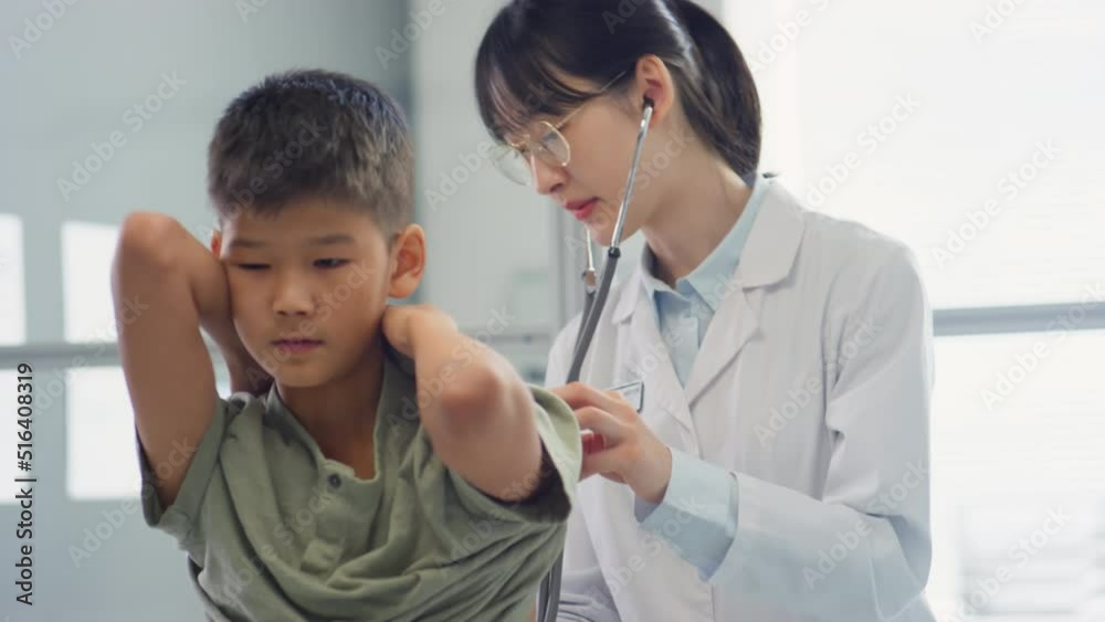 Asian female doctor examining boy with stethoscope and then showing thumb up to him during health checkup in clinic Asian female doctor examining boy with stethoscope and then showing thumb up to him during health checkup in clinic