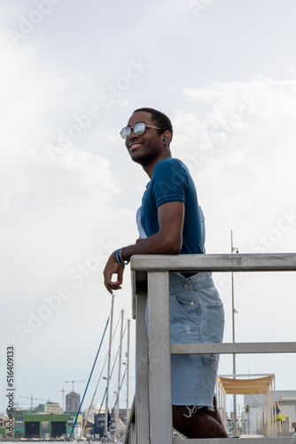 smiling black man leaning against the railing with sunglasses looking at the view © MarcoLatino