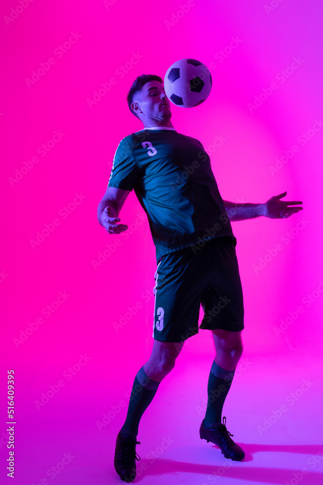 Caucasian male soccer player playing with football over neon pink lighting Caucasian male soccer player playing with football over neon pink lighting