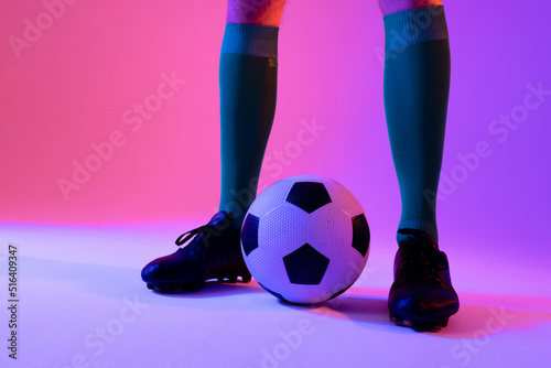 Caucasian male soccer player with football over neon pink lighting