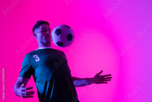 Caucasian male soccer player playing with football over neon pink lighting