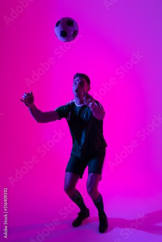 Caucasian male soccer player playing with football over neon pink lighting