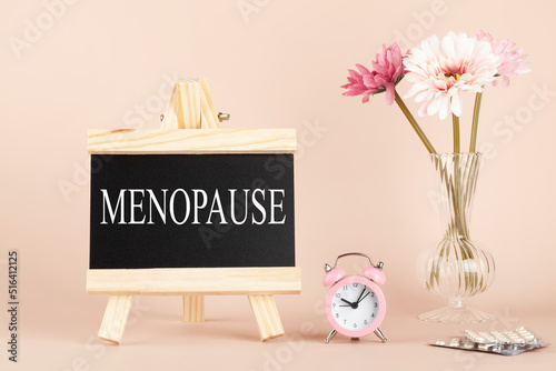 menopause word written on black board, flowers, clock and pills on beige background. women health and middle age concept. medicine, healthcare style photo