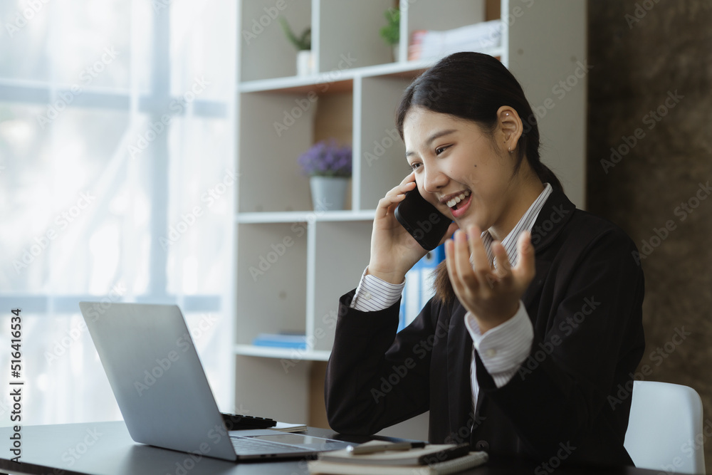 Asian woman talking on the phone, she is a salesperson in a startup company, she is calling customers to sell products and promotions. Concept of selling products through telephone channels. Asian woman talking on the phone, she is a salesperson in a startup company, she is calling customers to sell products and promotions. Concept of selling products through telephone channels.