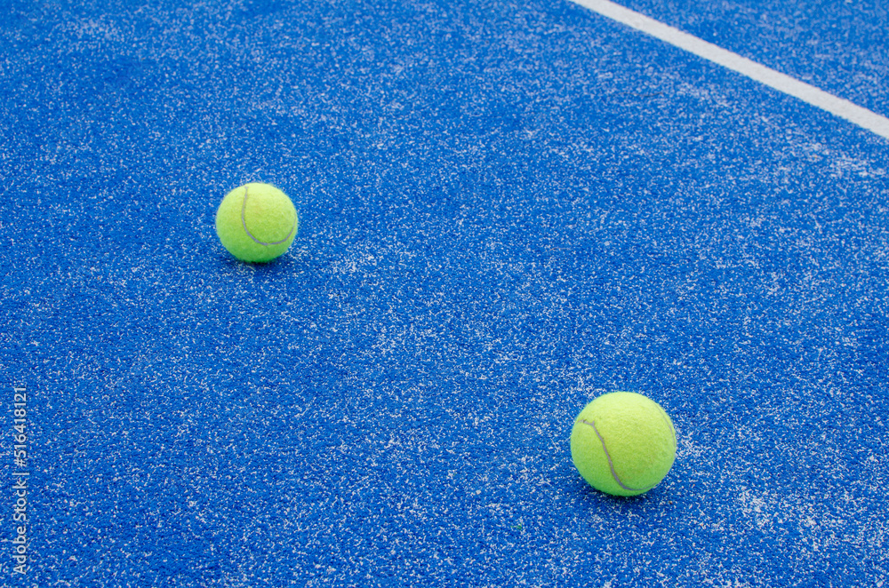 SELECTIVE FOCUS, TWO PADDLE TENNIS BALLS IN A BLUE TURF PADDLE TENNIS COURT