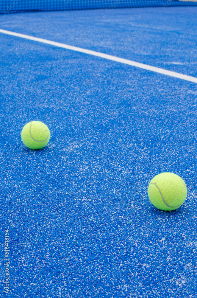 SELECTIVE FOCUS, TWO PADDLE TENNIS BALLS ON A BLUE PADDLE TENNIS COURT WITH SYNTHETIC GRASS