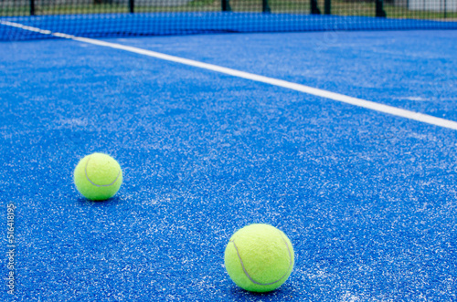 SELECTIVE FOCUS, TWO PADDLE TENNIS BALLS ON A BLUE PADDLE TENNIS COURT WITH SYNTHETIC GRASS © Vic