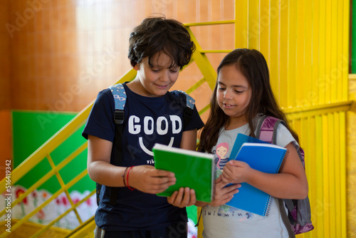 Two Caucasian primary school pupils talking amicably in the corridor before entering the classroom. First day back to school. Concept of learning, education and development in early childhood.