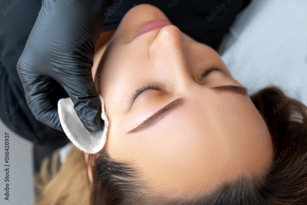 cleansing the model's skin with a cotton sponge after eyebrow tattooing  using a permanent makeup machine Stock Photo | Adobe Stock