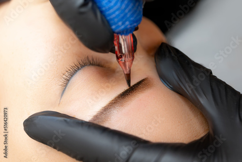close-up master makes eyebrow tattoo apply permanent makeup on the model's eyebrows
