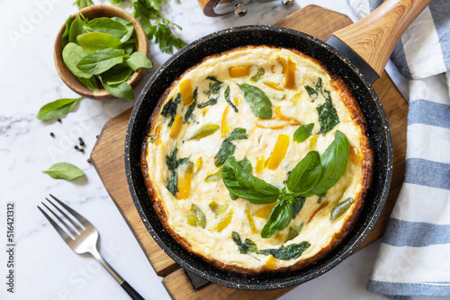 Spinach and cheese omelette. Frittata made of eggs, paprika and spinach in a frying pan on a marble countertop.