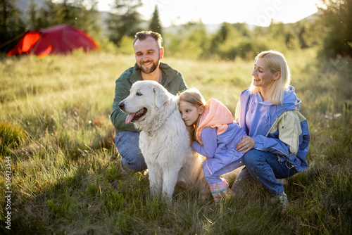 Portrait of a lovely couple with little girl and dog hug together while travel in the mountains. Young caucasian family spend summer vacation on nature