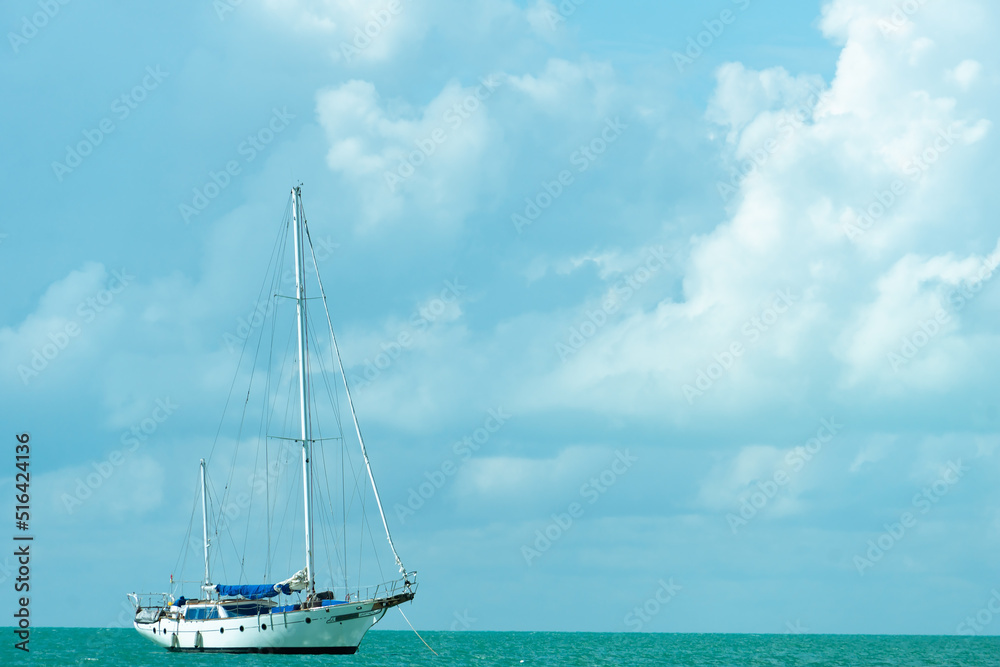 A yacht with a lowered sail against a cloudy sky. White sailboat on turquoise waves. Copy space.