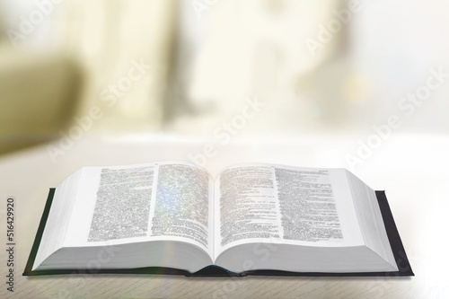 Open holy bible on a wooden table. Beautiful white wall background.