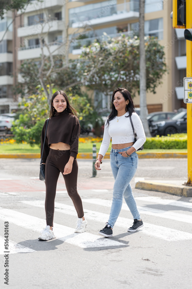Vertical photo of two friends walking across a pedestrian crossing in the street