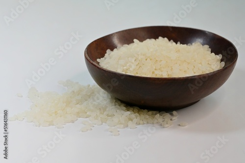 Coconut husk bowl filled with polished white Japanese short grain rice kernels, on white background photo