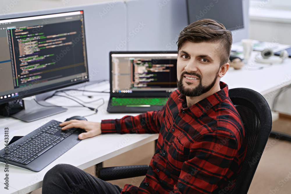 Computer programmer developer working in IT office, sitting at desk and coding, working on a project in software development company or startup.