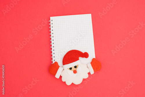 Christmas notebook wire binding blank template design idea. Santa Claus with red cap and winter gloves under notebook and against pastel pink background. Copy space for merry christmas message.