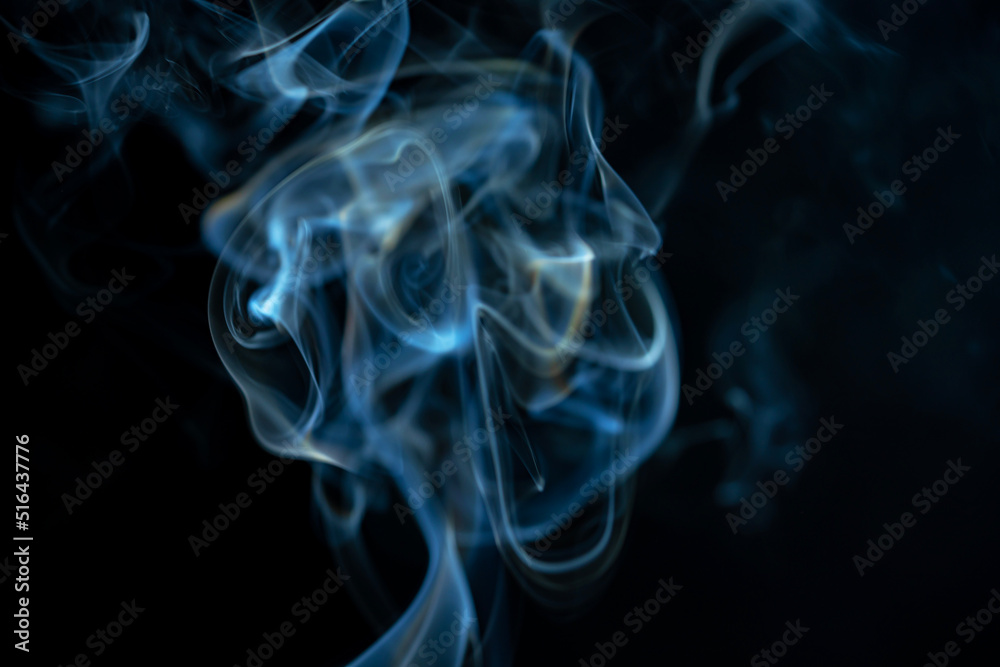 White blue cloud of smoke from smoking a cigar on an isolated black background. Fumes from smolder cigarette floating in the space. Smoke flying in the air and illuminated by light. Macro shot.