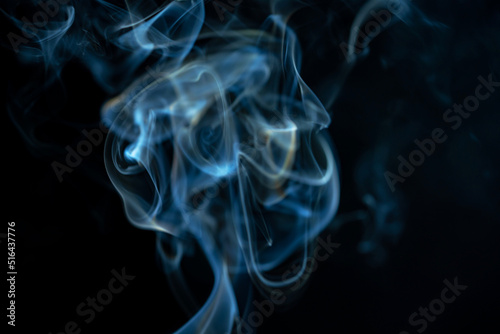 White blue cloud of smoke from smoking a cigar on an isolated black background. Fumes from smolder cigarette floating in the space. Smoke flying in the air and illuminated by light. Macro shot.