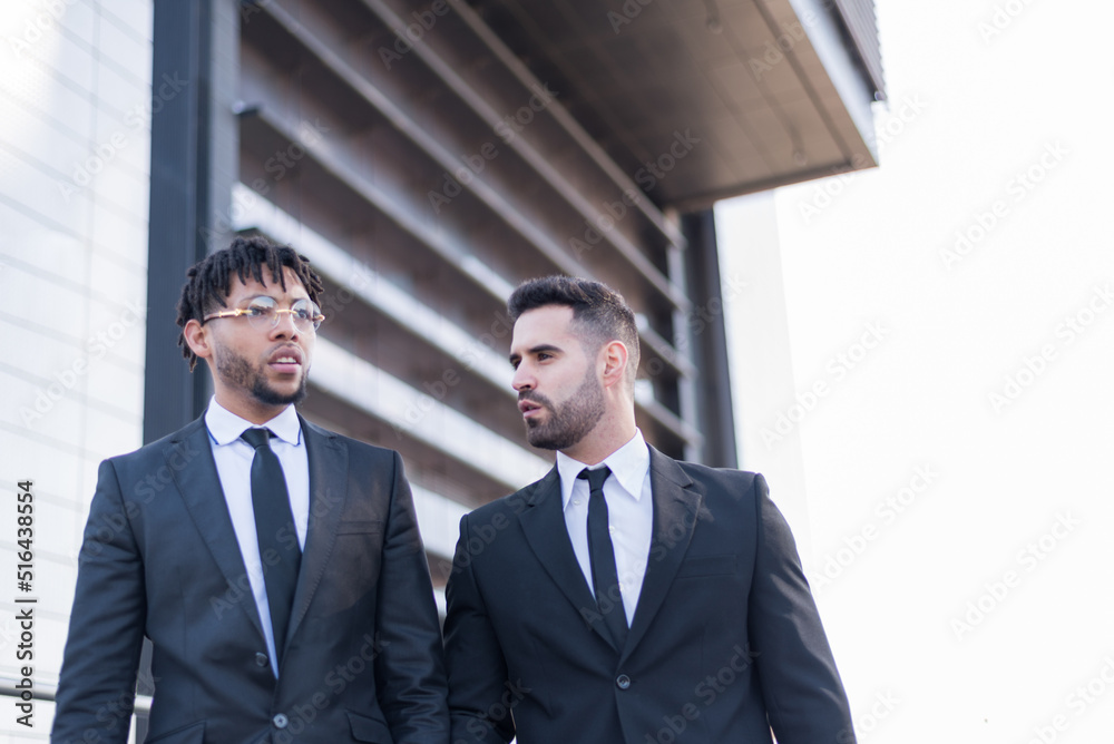businessmen wearing suits walking and smiling and talking outdoor in a business area. businessmen wearing suits walking and smiling and talking outdoor in a business area.
