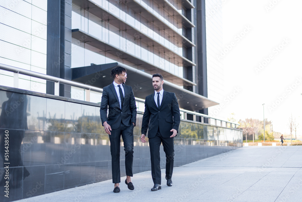 businessmen wearing suits walking and smiling and talking outdoor in a business area. businessmen wearing suits walking and smiling and talking outdoor in a business area.