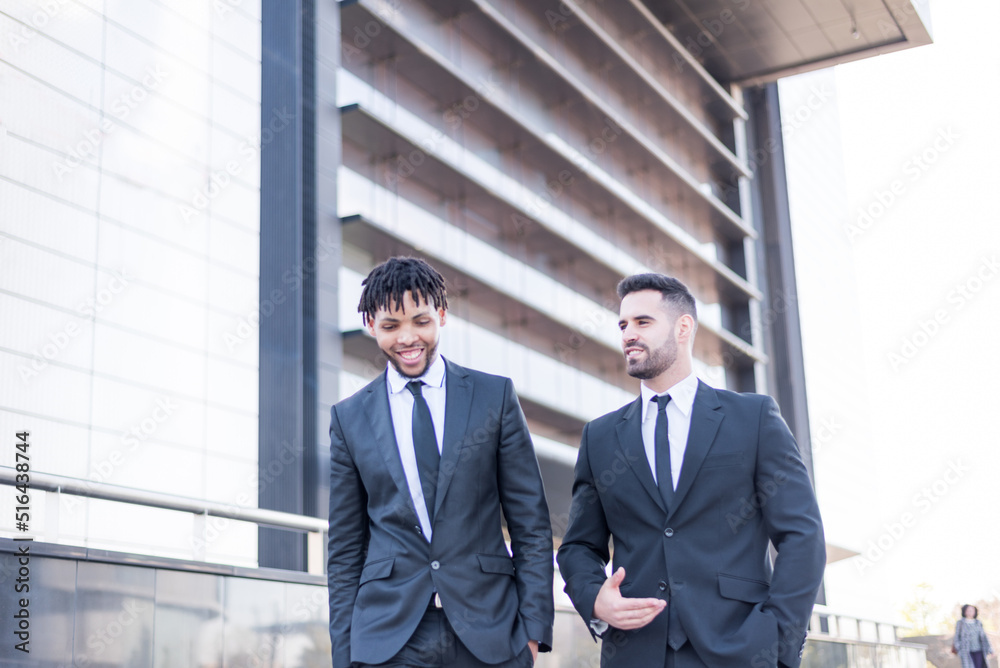 businessmen wearing suits walking and smiling and talking outdoor in a business area. businessmen wearing suits walking and smiling and talking outdoor in a business area.
