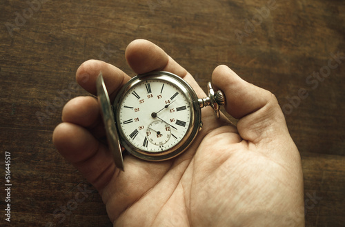 An elderly man's hand is holding a pocket watch. The passing time. A mechanical watch in a man's hand.
