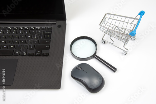 Laptop, magnifying glass, computer mouse and grocery basket on a white background. Items for business and buying goods online