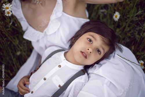 woman in a white dress with her son, a boy of 5 years old, lies in a chamomile field at sunset in summer.