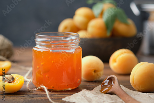 Jar of homemade apricot jam and ripe apricot fruits on kitchen table.