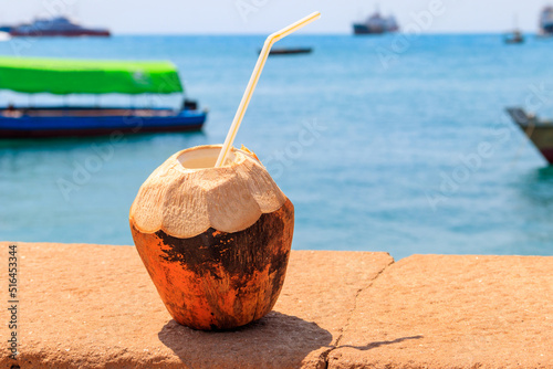 Fresh tropical coconut cocktail with drinking straw by ocean in Stone Town, Zanzibar, Tanzania
