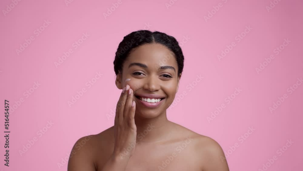 Facial care. Young pretty african american woman applying pampering cream on cheek, moisturizing her skin, slow motion Facial care. Young pretty african american woman applying pampering cream on cheek, moisturizing her skin, slow motion